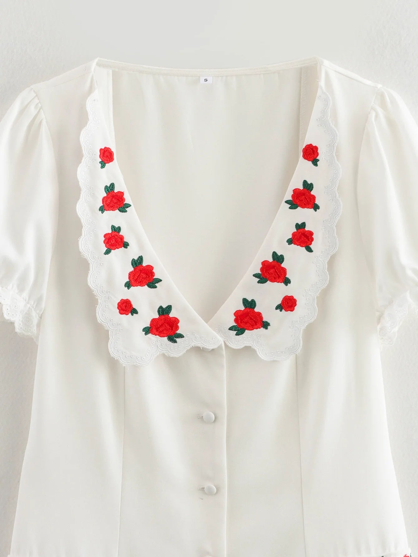 White blouse with red floral embroidery on a white background