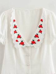 White blouse with red floral embroidery on a white background