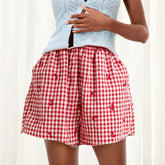 Model displaying red plaid shorts with cherry print and an elastic high waist.