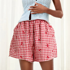 Model displaying red plaid shorts with cherry print and an elastic high waist.