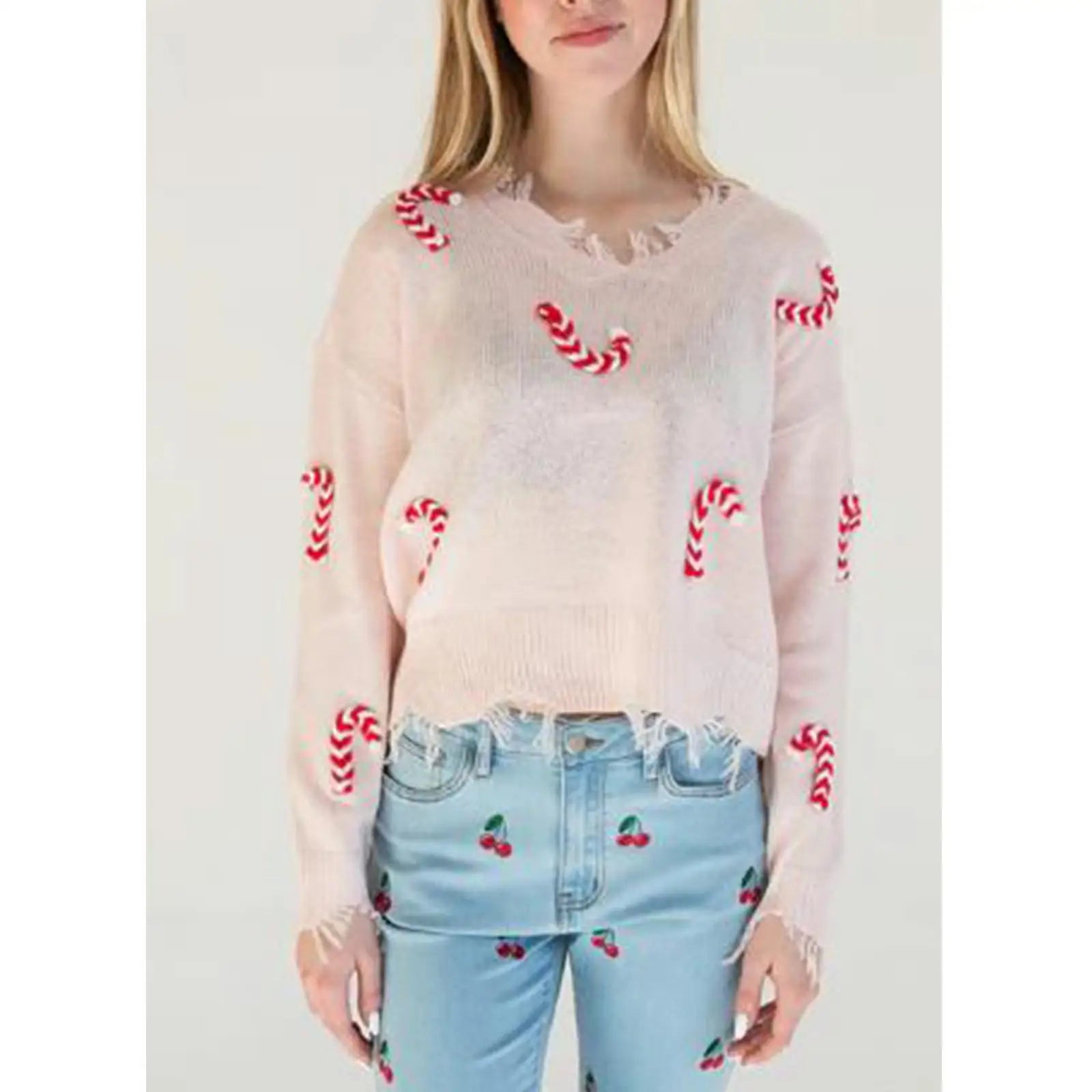 Person wearing a sheer pink sweater with red patterns and light blue jeans with cherry patterns.