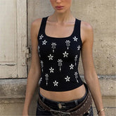 Black tank top with white floral patterns worn by a person against a stone wall.