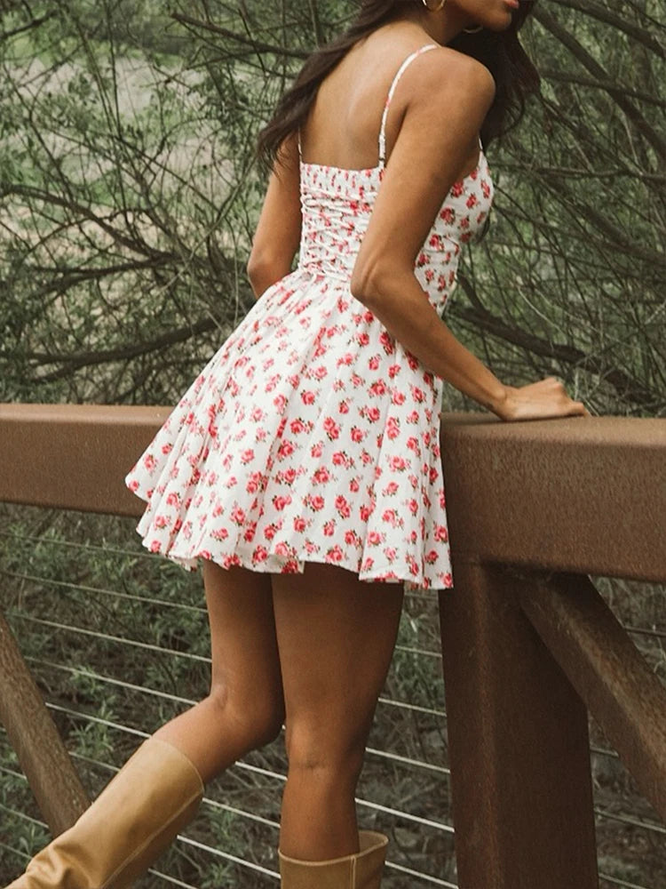 Woman wearing a white floral dress standing outdoors near a wooden railing.