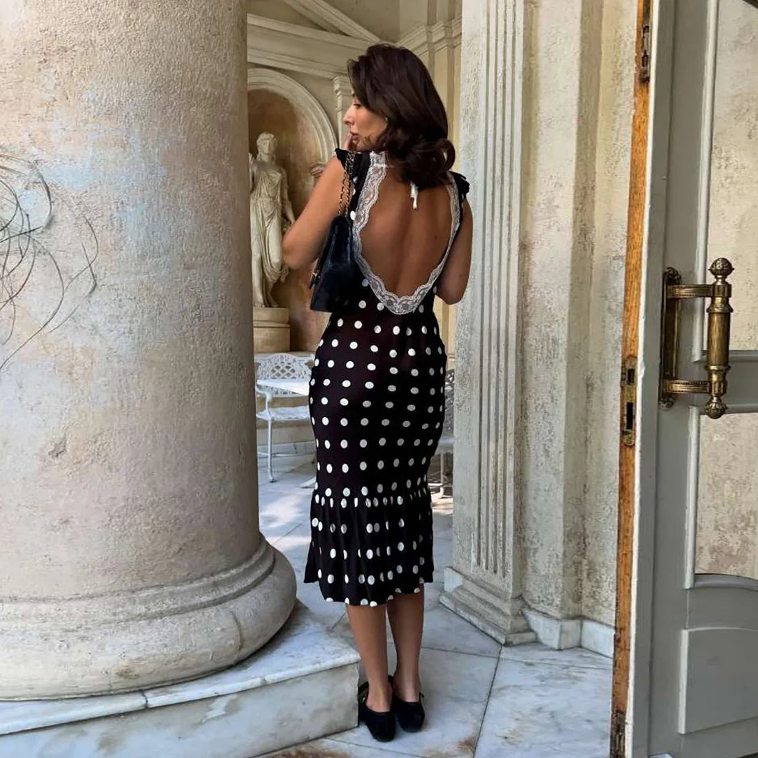 Woman in a black and white polka dot dress standing in an elegant outdoor setting.