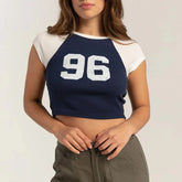 Person wearing a navy and white crop top with the number 96 on a plain background