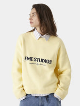 Person wearing a light yellow sweater with 'EME STUDIOS' text on a white background