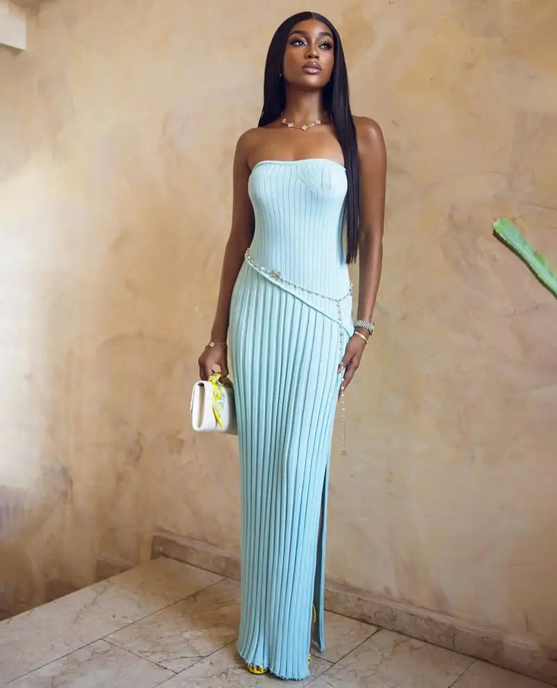 Woman in a light blue strapless dress with a slit, standing against a beige wall.