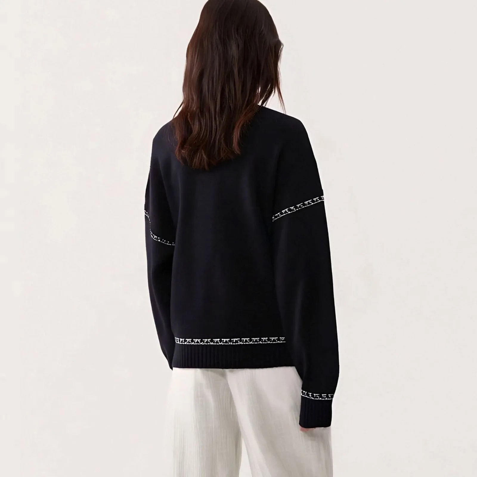 Person wearing a black sweater with white patterns on a plain background