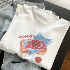 Folded white t-shirt with tomato graphic design on a dark surface