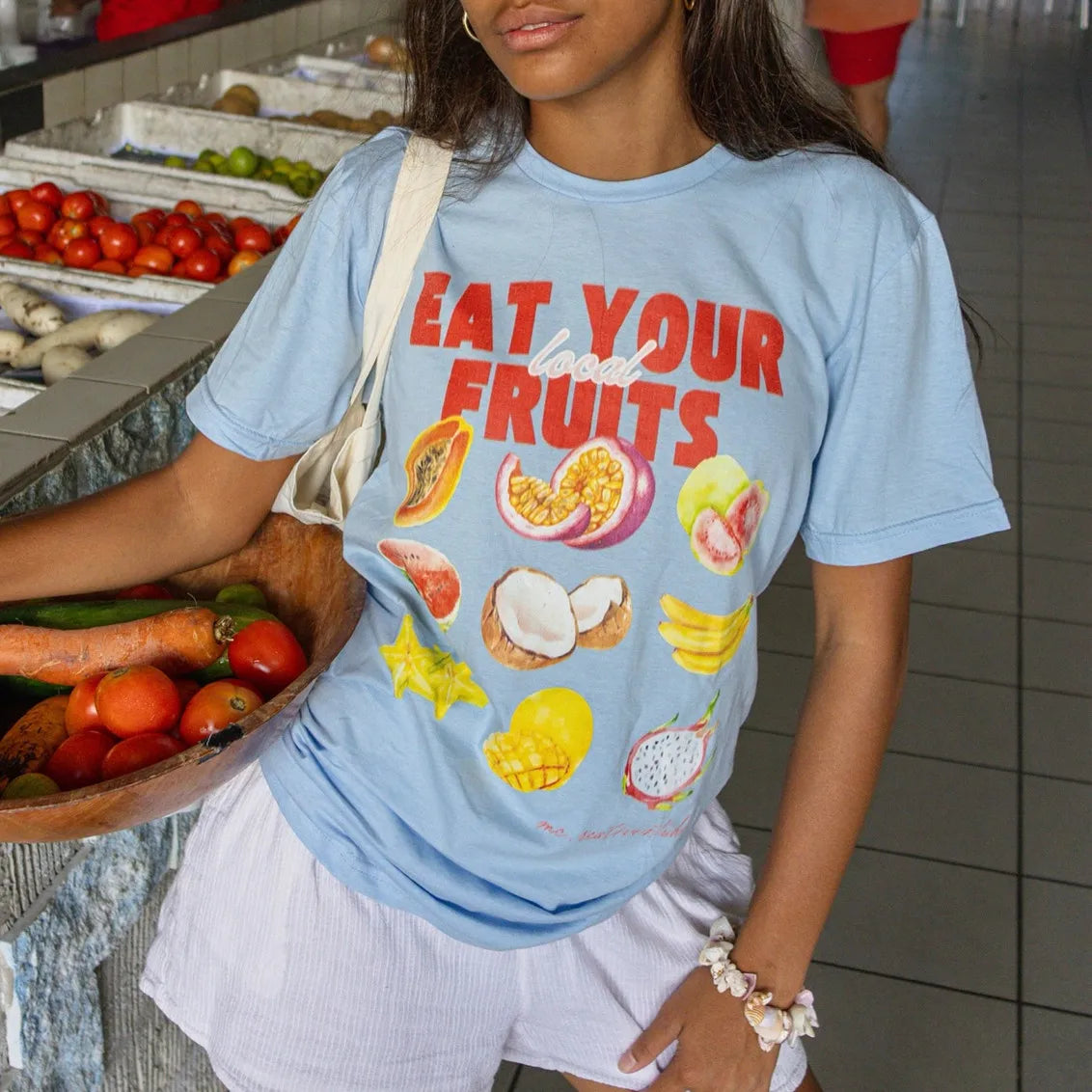 Person wearing a blue t-shirt with fruit illustrations and text in a market setting