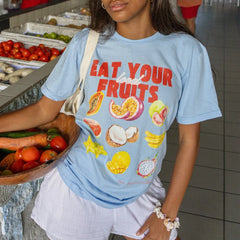 Person wearing a blue t-shirt with fruit illustrations and text in a market setting