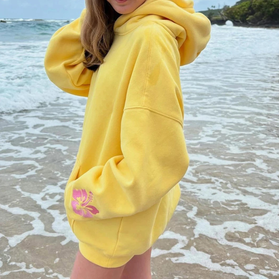 Person wearing a yellow hoodie with a pink flower design on a beach