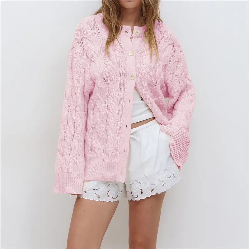 Person wearing a pink knitted cardigan over a white outfit on a plain background