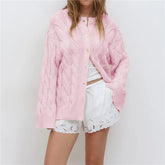 Person wearing a pink knitted cardigan over a white outfit on a plain background