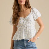 Woman wearing a floral blouse with ruffled details against a beige background