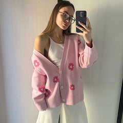 Woman wearing a pink cardigan with floral patterns, taking a mirror selfie.