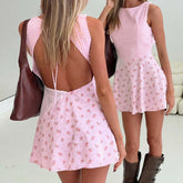 Woman wearing a pink floral dress with a back cutout, holding a brown bag.