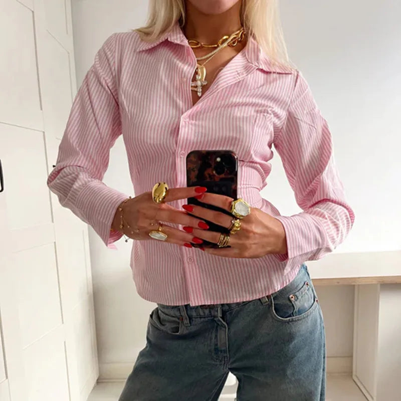 Person wearing a pink striped shirt and jeans, holding a phone with a white background