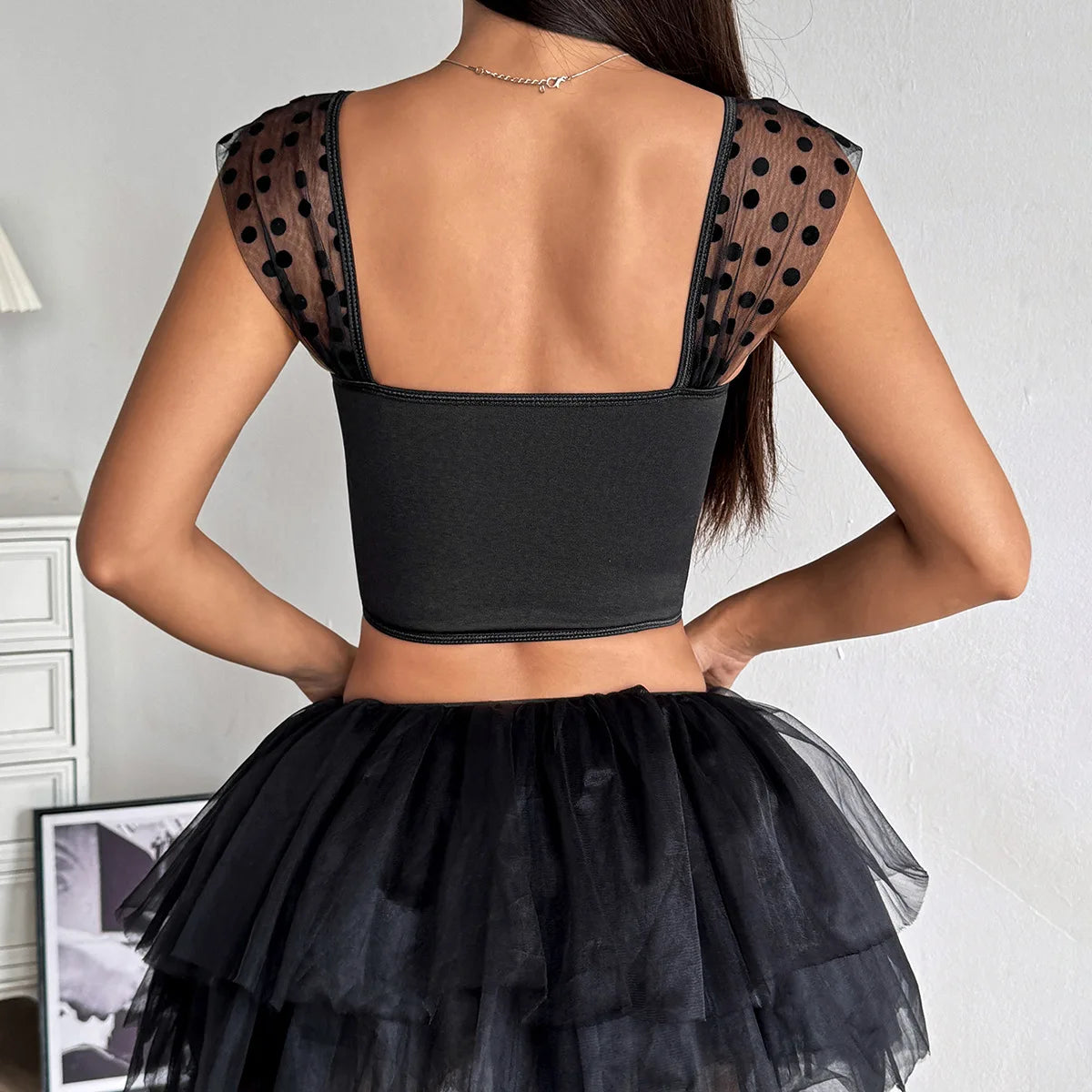 Black crop top with sheer polka dot sleeves and a black tulle skirt on a plain background