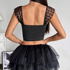 Black crop top with sheer polka dot sleeves and a black tulle skirt on a plain background