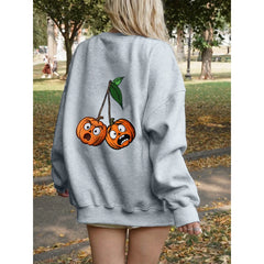 Person wearing a gray sweatshirt with cartoon cherries on the back in an outdoor setting.