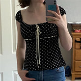 Person wearing a black polka dot top taking a mirror selfie.