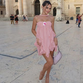 Woman in a pink dress standing in an outdoor setting with classical architecture.