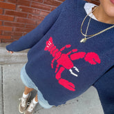 Person wearing a navy blue sweater with a red lobster design, standing on a sidewalk.