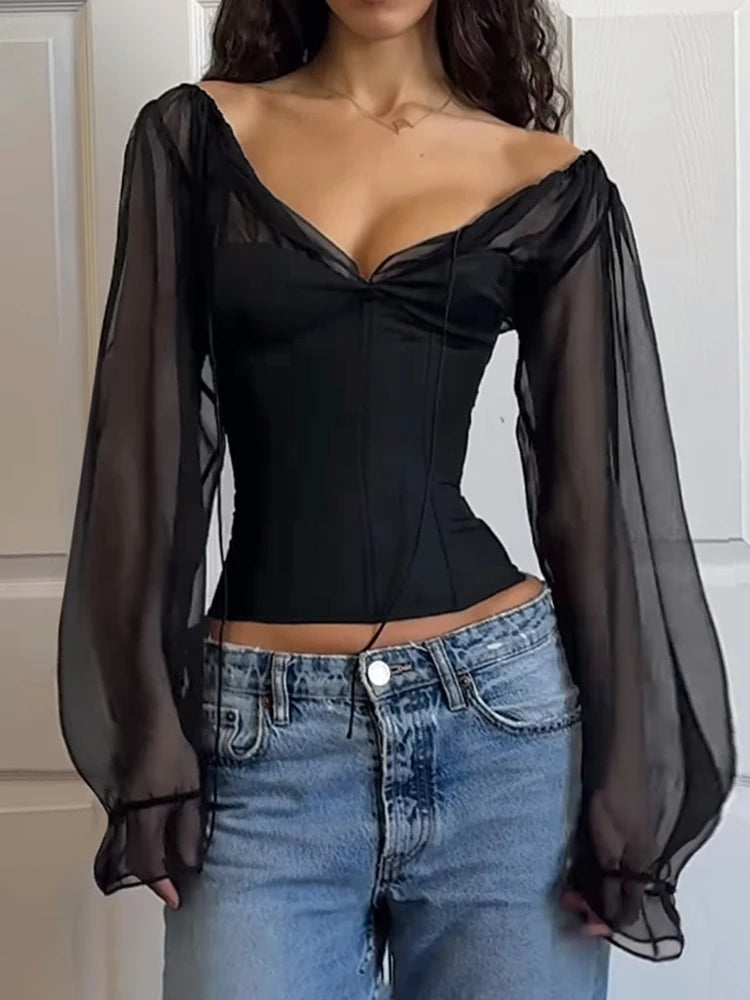 Black top with sheer sleeves and blue jeans against a neutral background