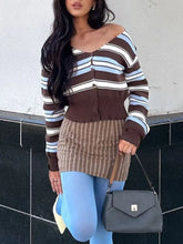Woman wearing a striped sweater and skirt with a gray handbag against a white wall.