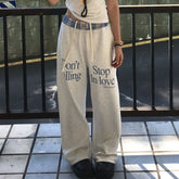 Person wearing light-colored sweatpants with text, standing on a tiled floor.