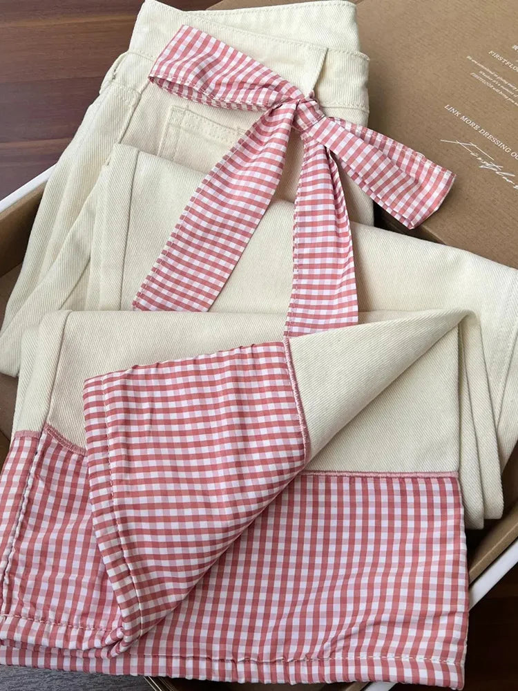 jeans with a pink gingham checkered ribbon on top, placed inside a cardboard box.