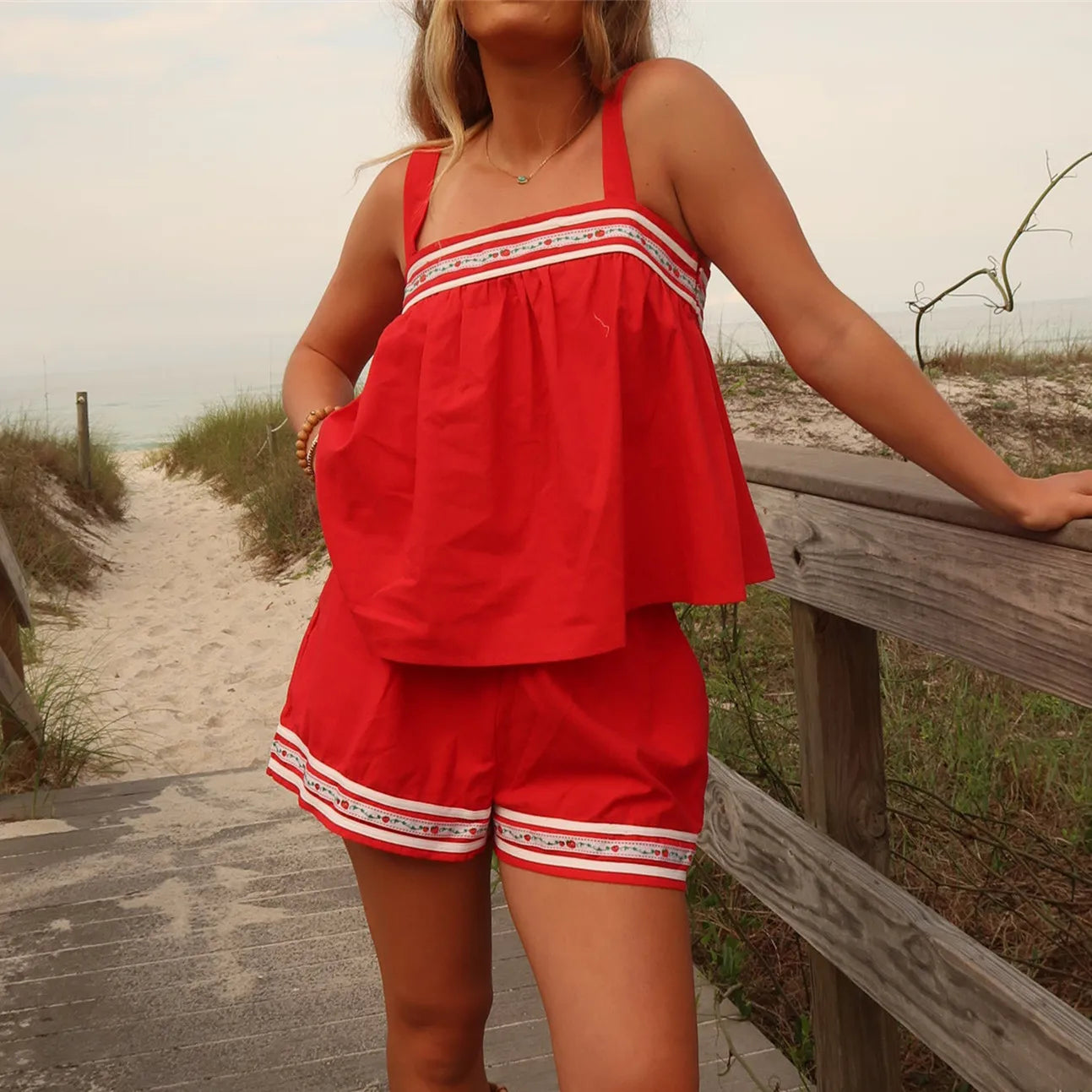 Woman in a red outfit standing on a sandy path with grass and a wooden railing.