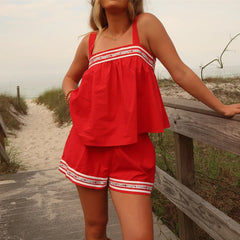 Woman in a red outfit standing on a sandy path with grass and a wooden railing.