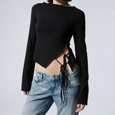 Person wearing a black long-sleeve crop top with cut-out design and blue jeans on a light gray background