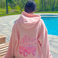 Person wearing a pink hoodie with a graphic design by a pool