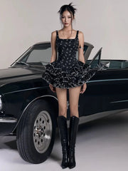 Woman in a black dress and knee-high boots standing in front of a black car.
