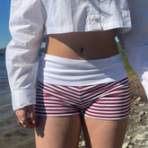 Person wearing a white shirt and red and white striped shorts by a body of water.