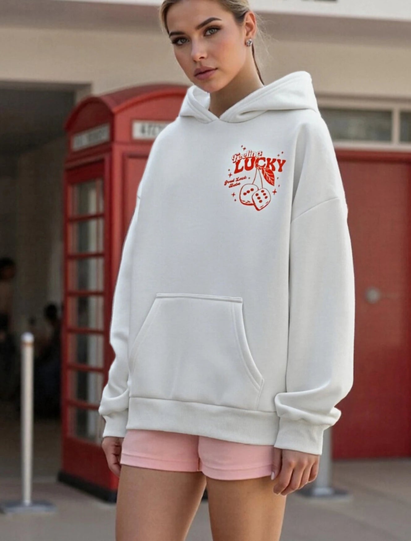 Woman wearing a white hoodie with red text and pink shorts in an urban setting.