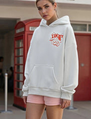 Woman wearing a white hoodie with red text and pink shorts in an urban setting.