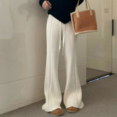Person wearing white ribbed pants and brown shoes, holding a brown bag indoors.