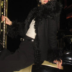 Person wearing a black fur coat sitting on a car at night.