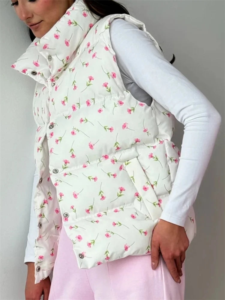 Person wearing a floral patterned puffer vest over a white shirt and pink pants on a plain background