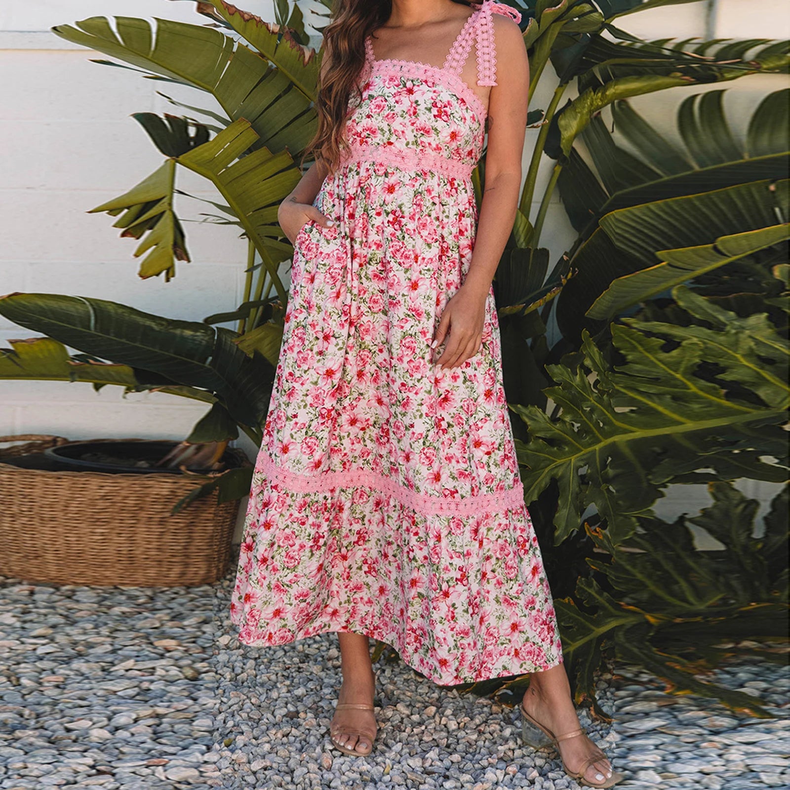 Woman wearing a pink floral dress standing in front of green plants- front view