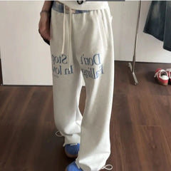 White sweatpants with text worn by a person on a wooden floor.