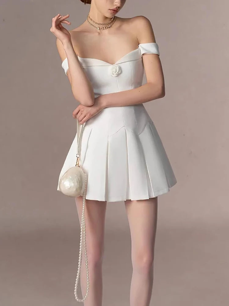 Woman wearing a white off-shoulder dress with a matching handbag against a beige background