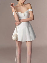 Woman wearing a white off-shoulder dress with a matching handbag against a beige background