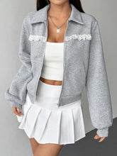 Person wearing a gray jacket with lace details and a white outfit on a plain background