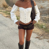 Person wearing a white off-shoulder top and brown shorts with a belt, standing on a road.