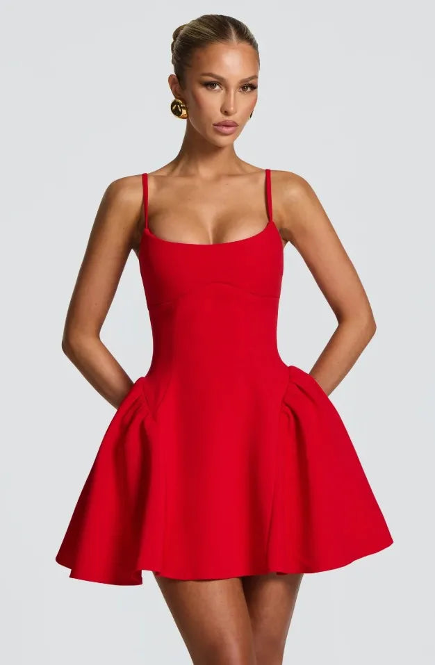 A woman modeling a bright red sleeveless mini dress with thin shoulder straps, a fitted bodice, and a flared skirt against a light gray studio background.
